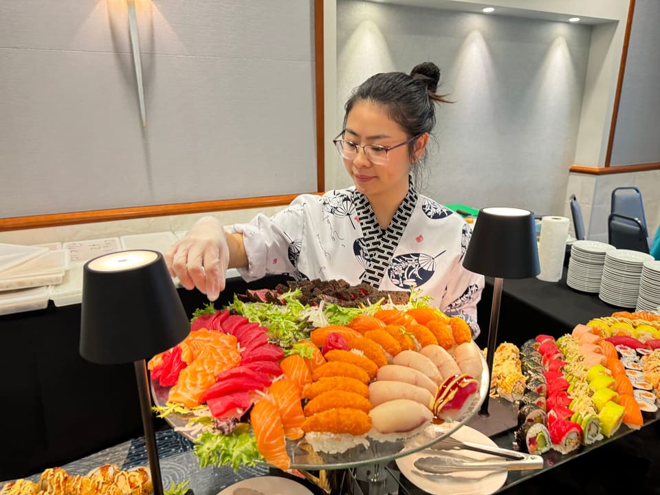 Ying Jein in chef's whites at a catering event, finishing a tiered sashimi and nigiri display by hand.