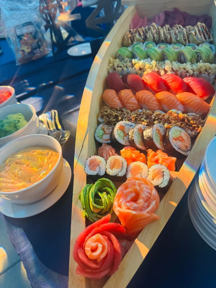 A wooden sushi boat filled end to end with nigiri, maki and rolls, finished with roses folded from salmon, tuna and avocado.