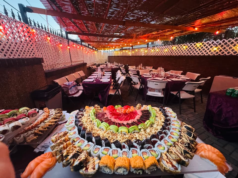 A circular sushi platter set out on a service table, with the event's laid tables, chairs and string lights behind it.