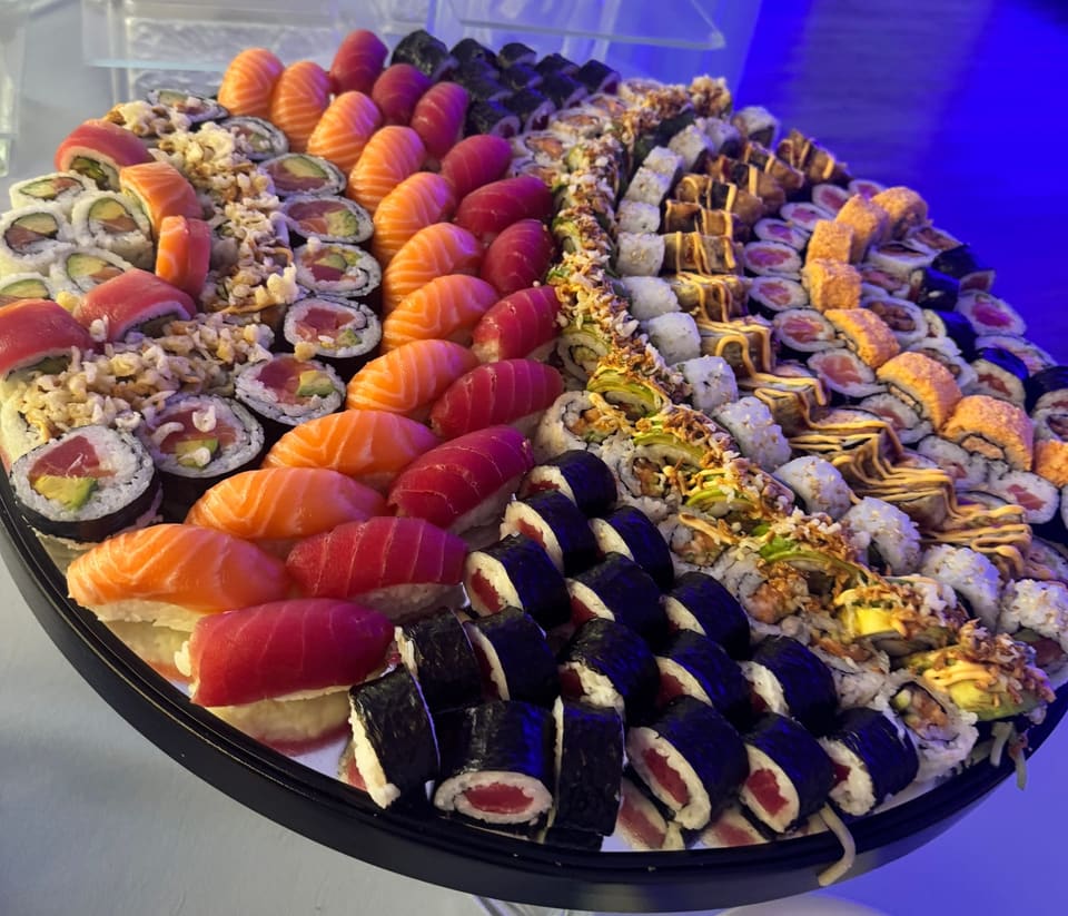 A large oval sushi platter, arranged in curved rows: salmon and tuna nigiri, maki, rainbow rolls and crisp-topped rolls finished with sauce.