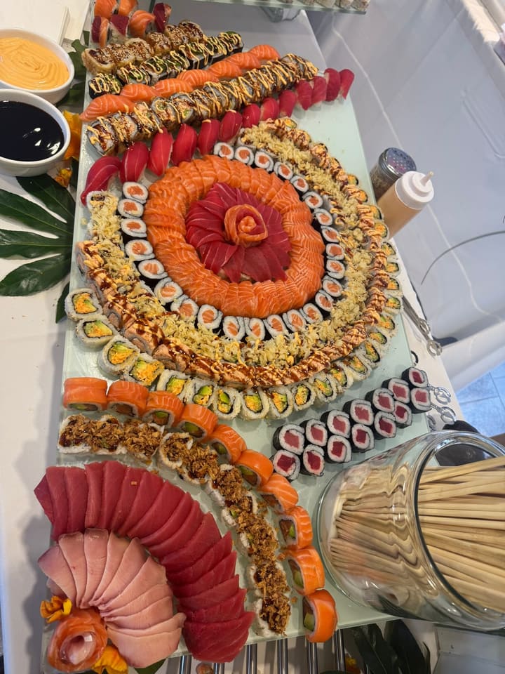 A long glass platter laid out as a spiral of salmon and tuna around a rose of tuna at the centre, ringed by maki and crisp-topped rolls, with a fan of sashimi alongside.